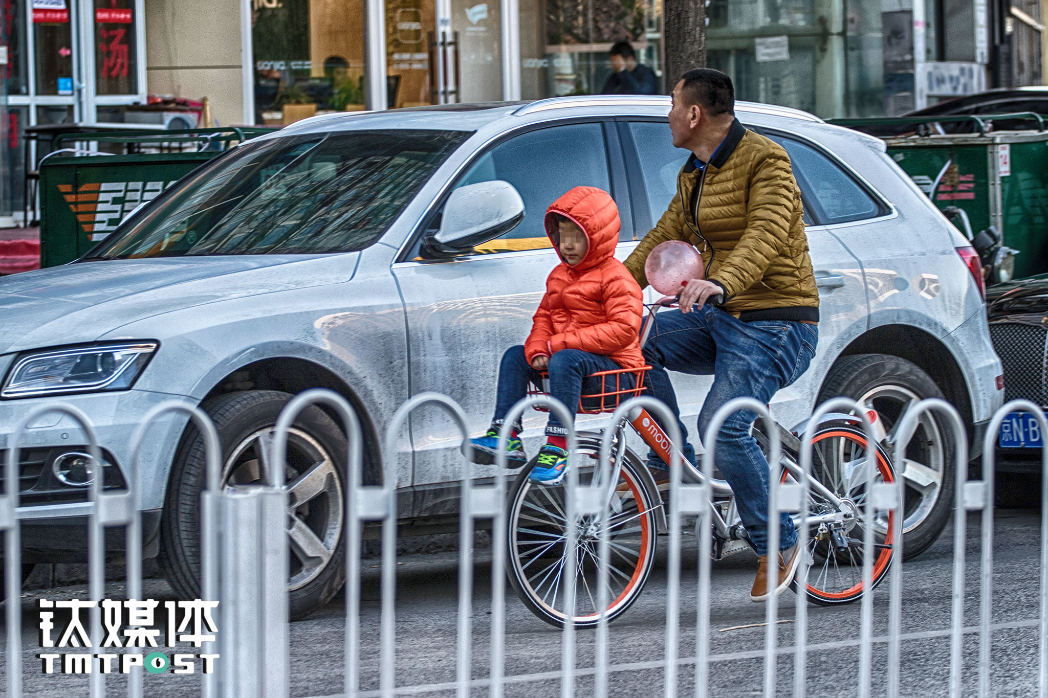国美餐饮街，一名成年男子在骑行中让孩子坐在摩拜单车的车篮里。
