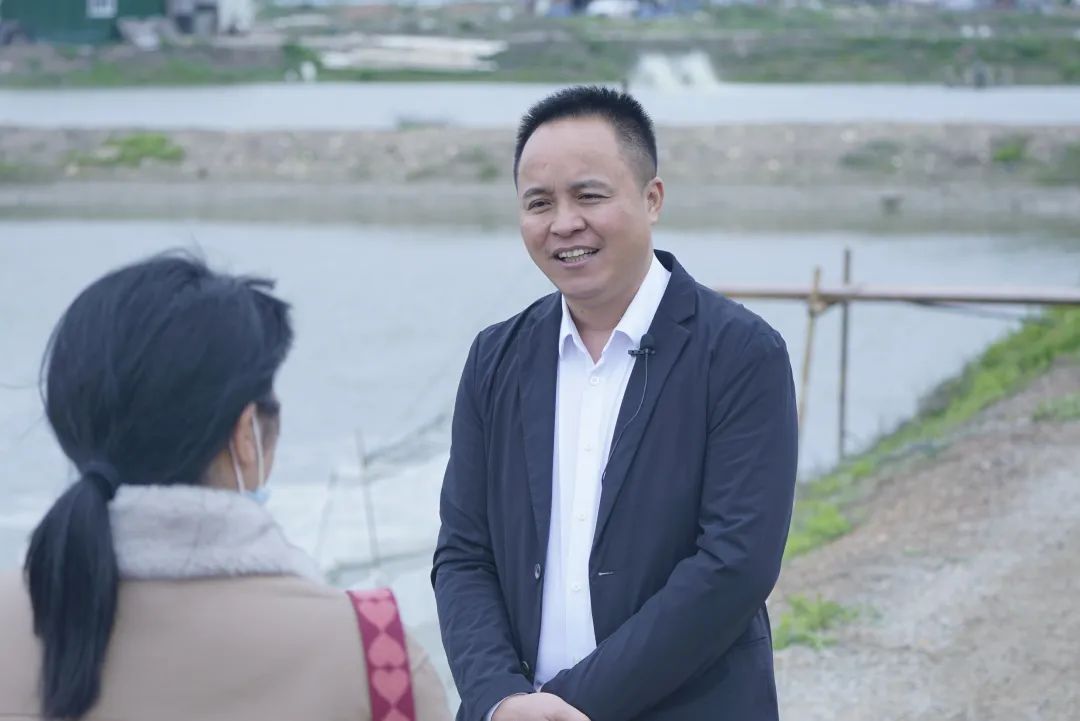 倪朝捷在鳗鱼养殖田边与来访者交谈