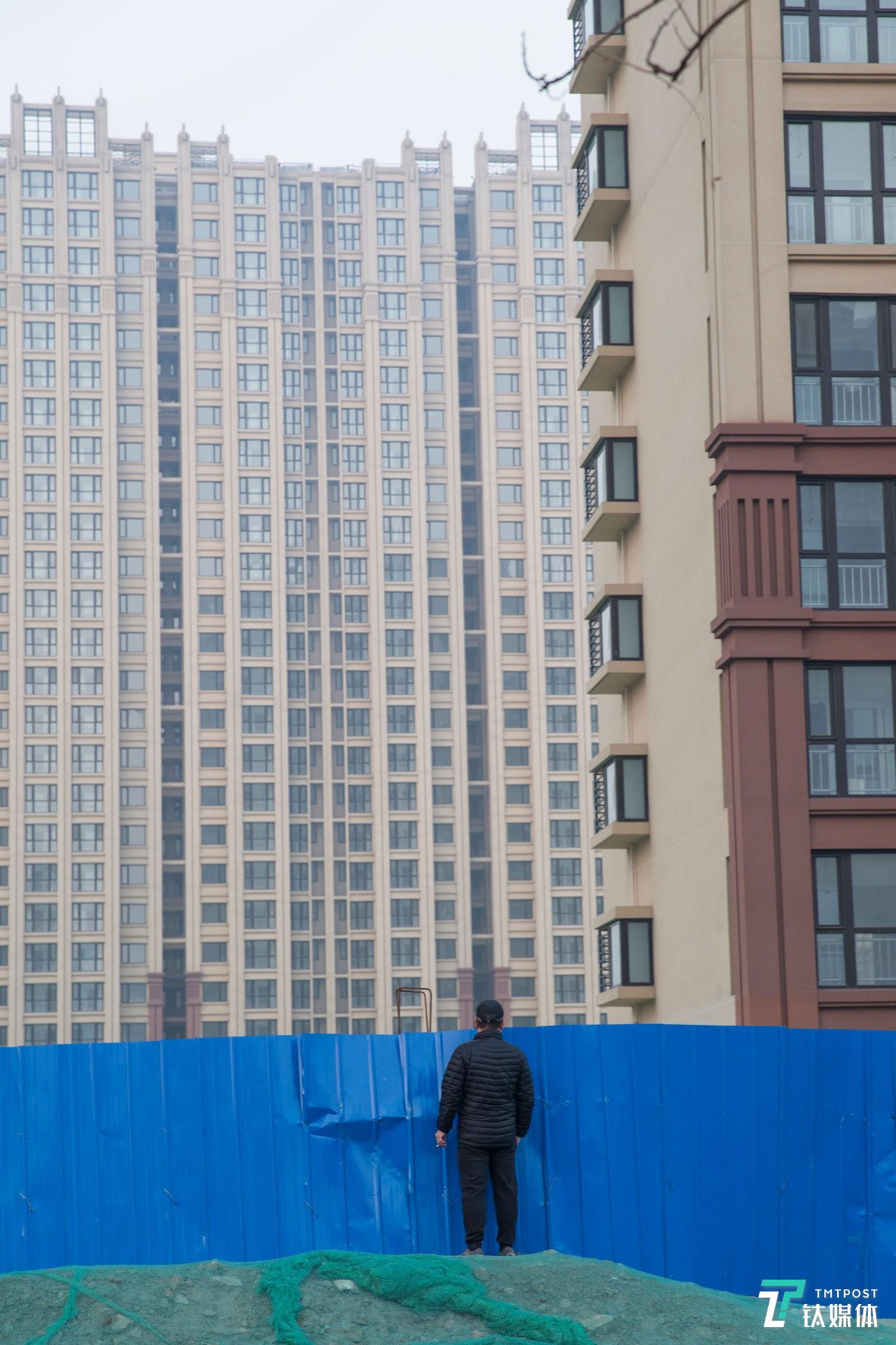 楼市观望者。北京通州，一名路人越过工地挡板望向一处住宅工地。