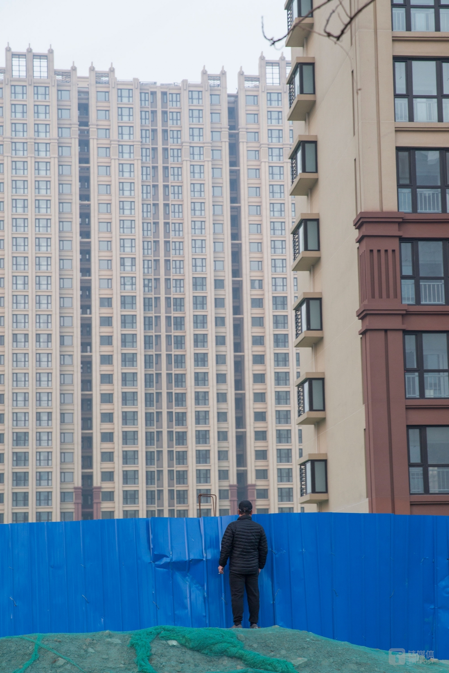 楼市观望者。北京通州，一名路人越过工地挡板望向一处住宅工地。